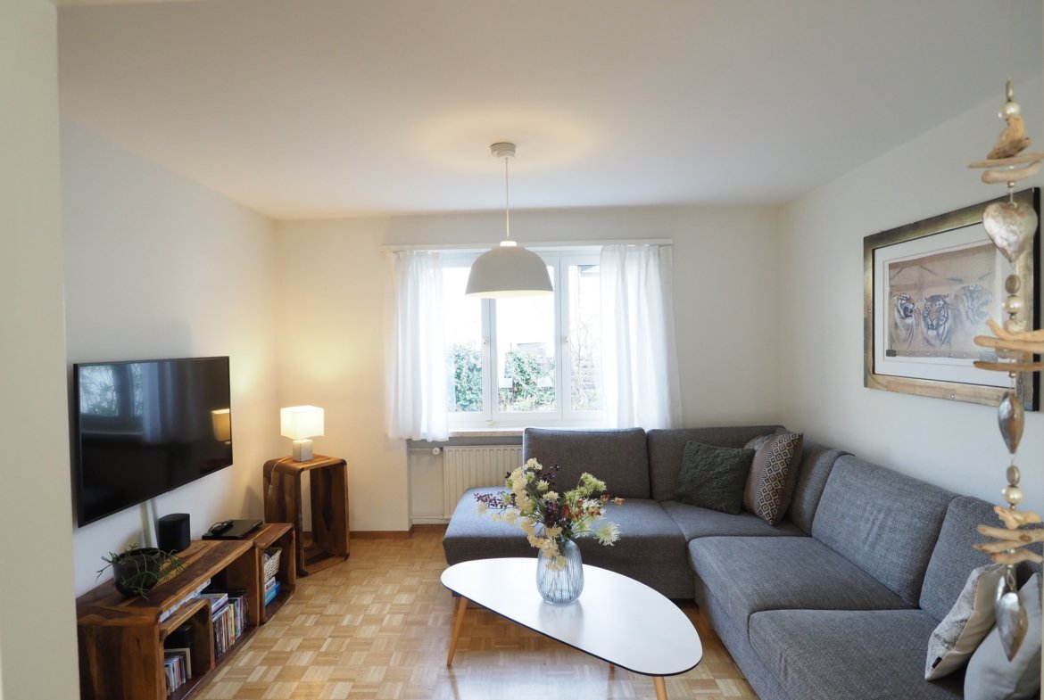 Heller Wohnraum mit grauer Eckcouch und TV