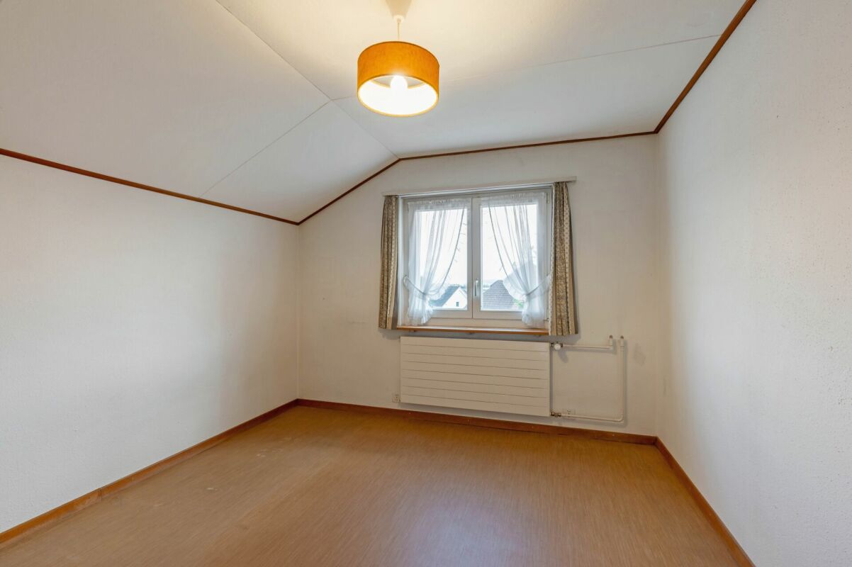Leerer Dachzimmer-Raum mit Fenster und Heizung