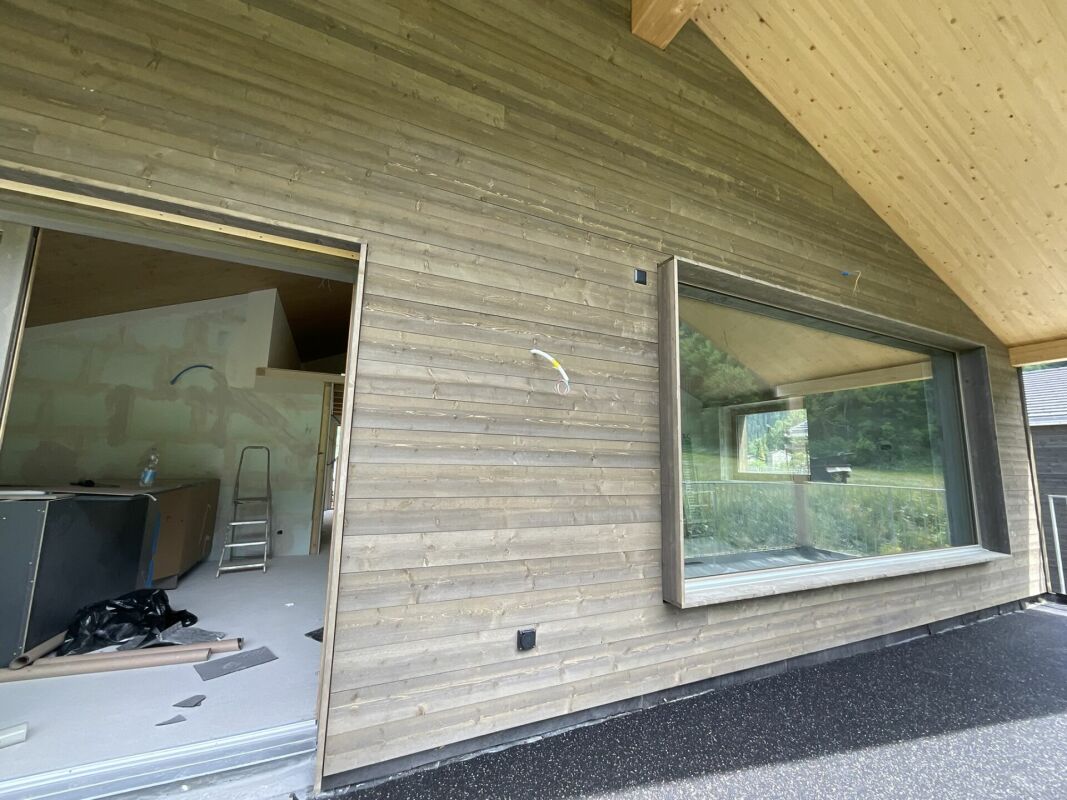 Holzfassade mit großem Fenster und offenem Innenausbau