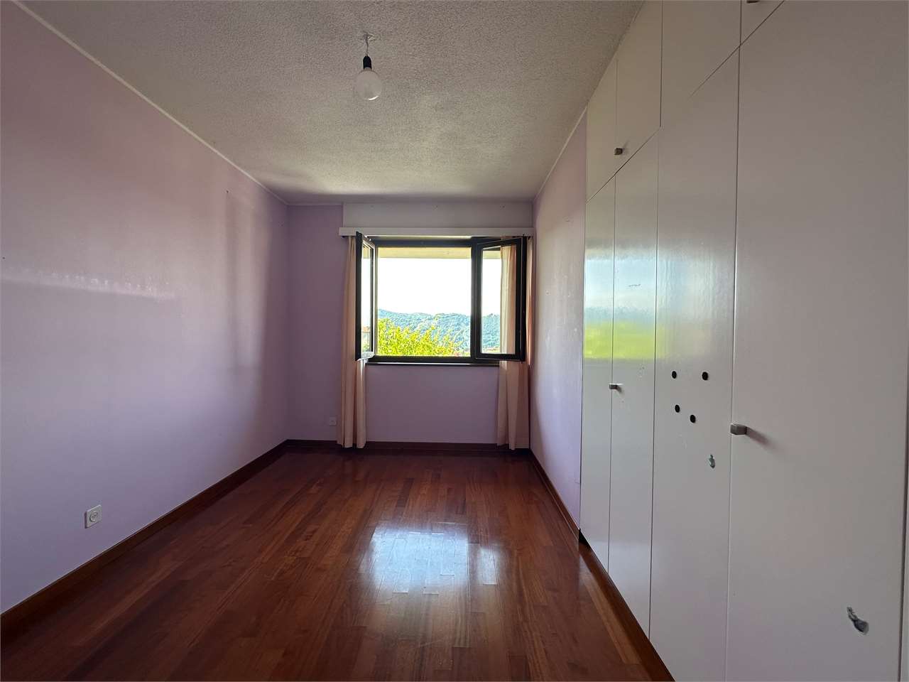 Leeres Schlafzimmer mit Einbauschrank und Blick ins Grüne