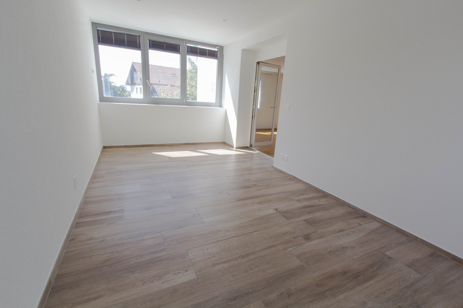 Helles, leerstehendes Zimmer mit Holzoptik-Boden und großem Fenster