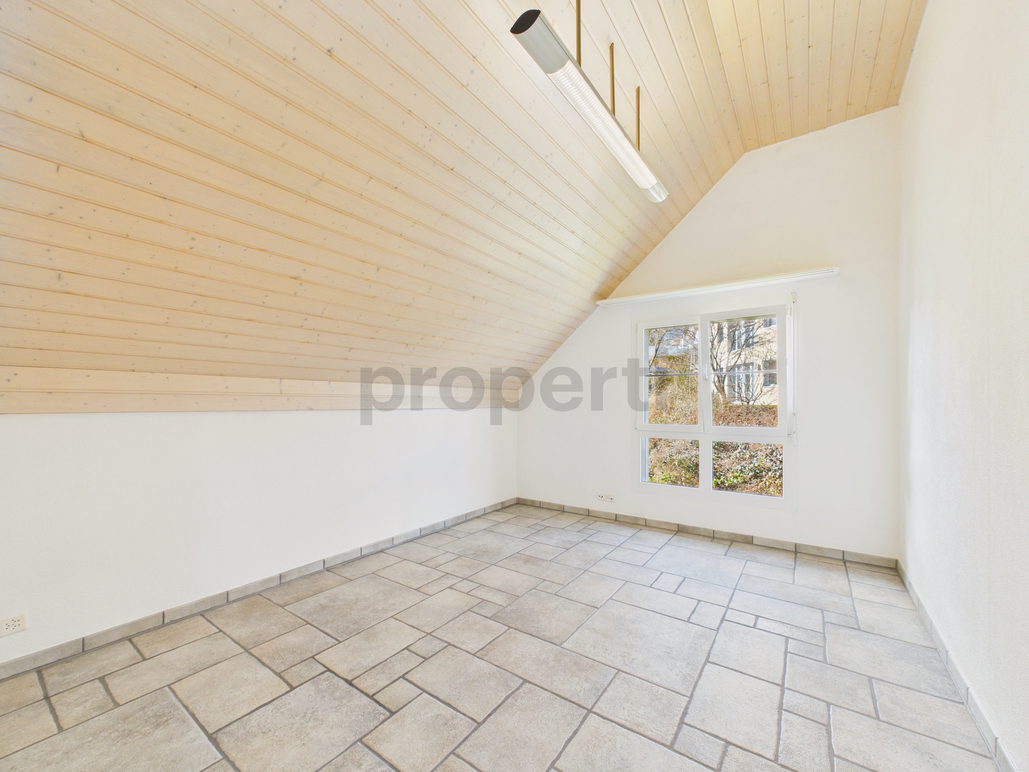 Heller leerer Raum mit schräger Holzdecke und Fliesenboden