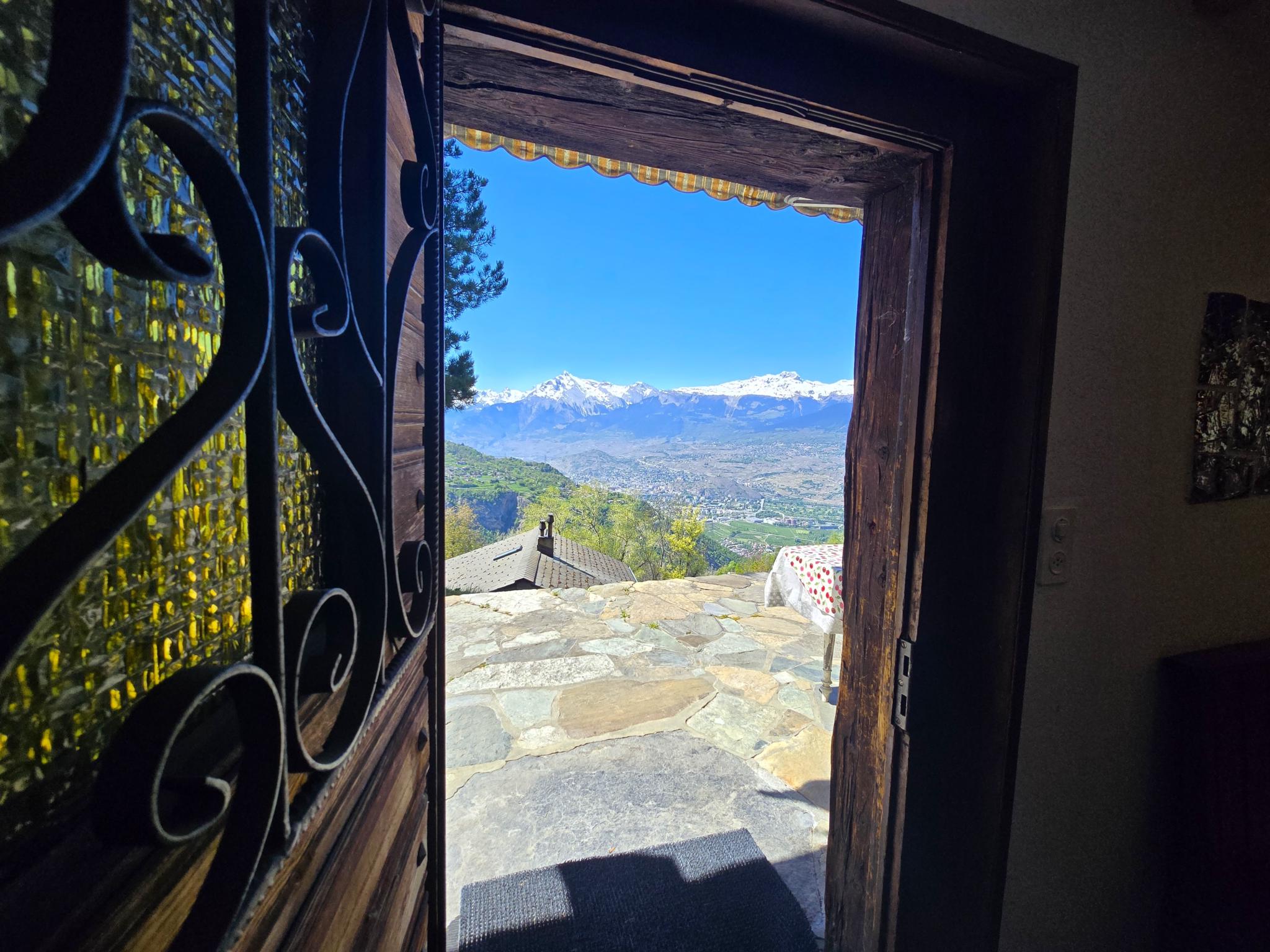 Blick von einer offenen Eingangstür auf eine Terrasse mit Bergpanorama