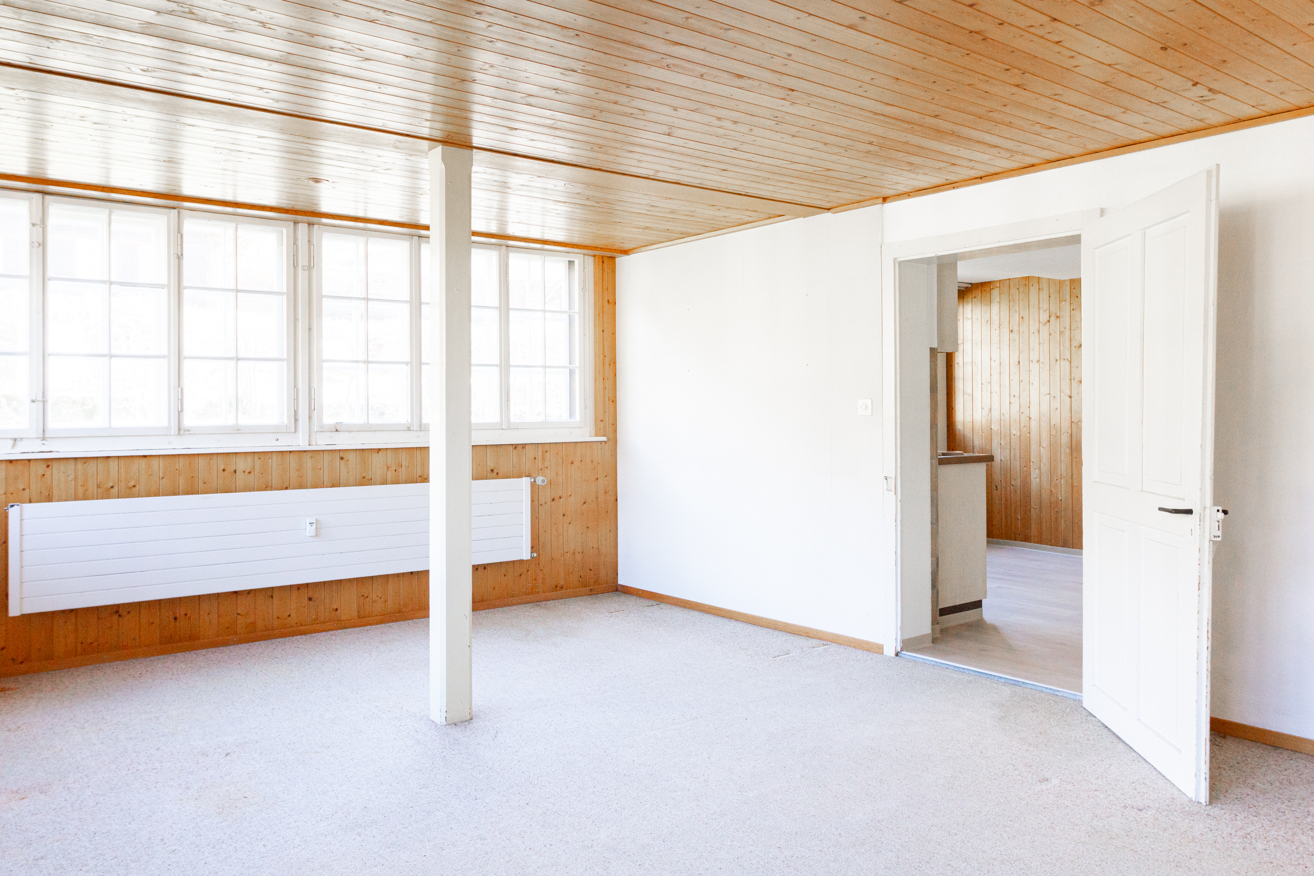 Heller leerer Wohnraum mit Holzdecke und großen Fenstern