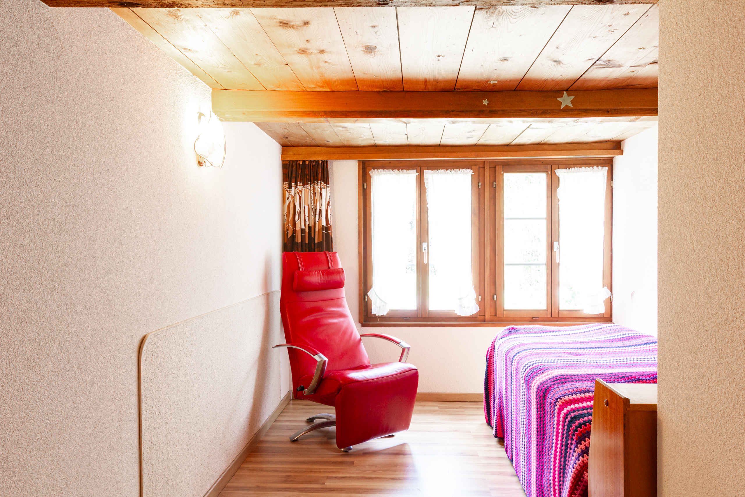 Helles Schlafzimmer mit Holzdecke und rotem Sessel