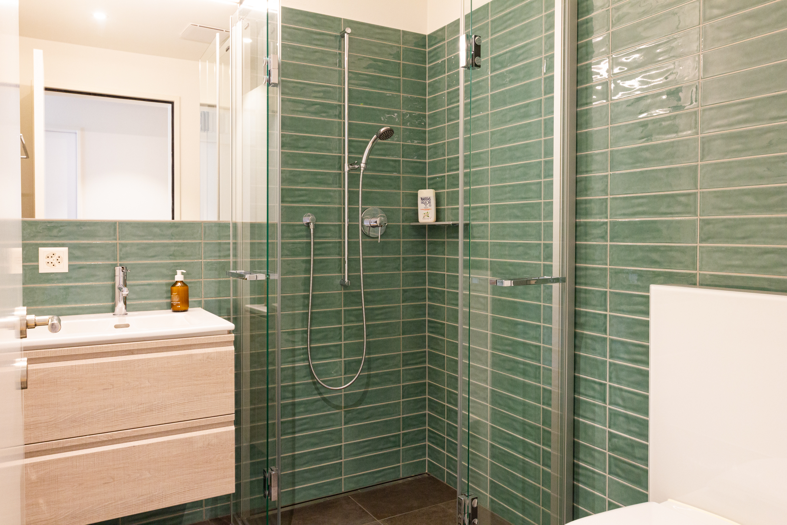 Modernes Badezimmer mit grüner Fliesenwand und Glasdusche