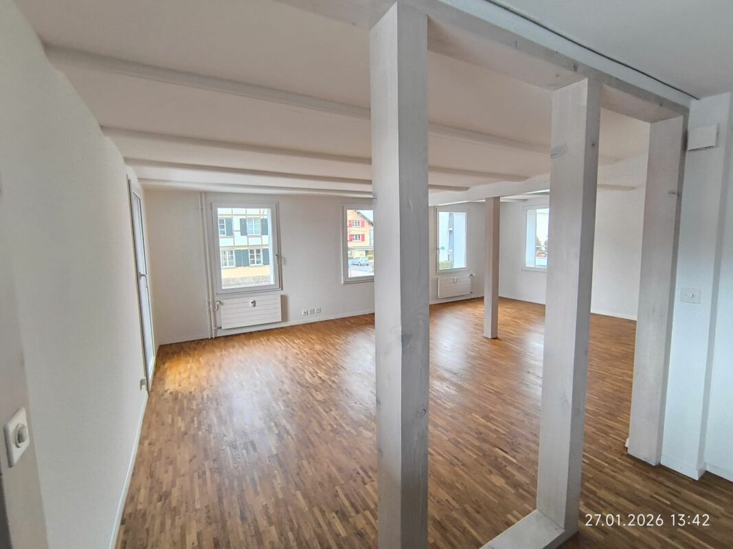 Heller leerer Innenraum mit Holzboden und sichtbaren Stützen
