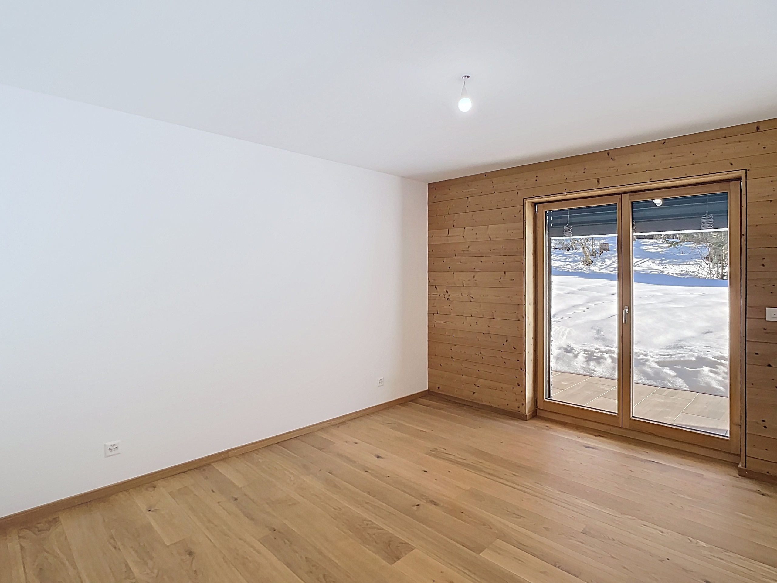 Leeres Schlafzimmer mit Holzakzenten und Blick ins Schneegebiet
