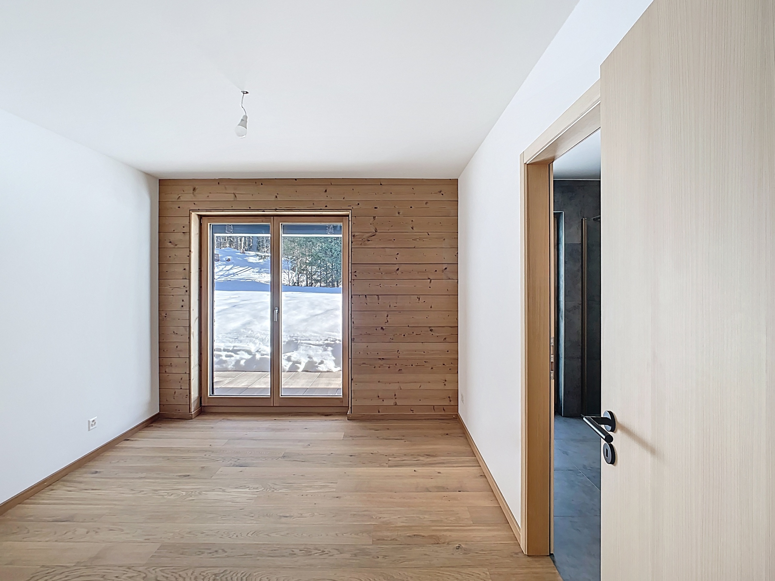 Helles Zimmer mit Holzverkleidung und Blick ins Schneelandschaft