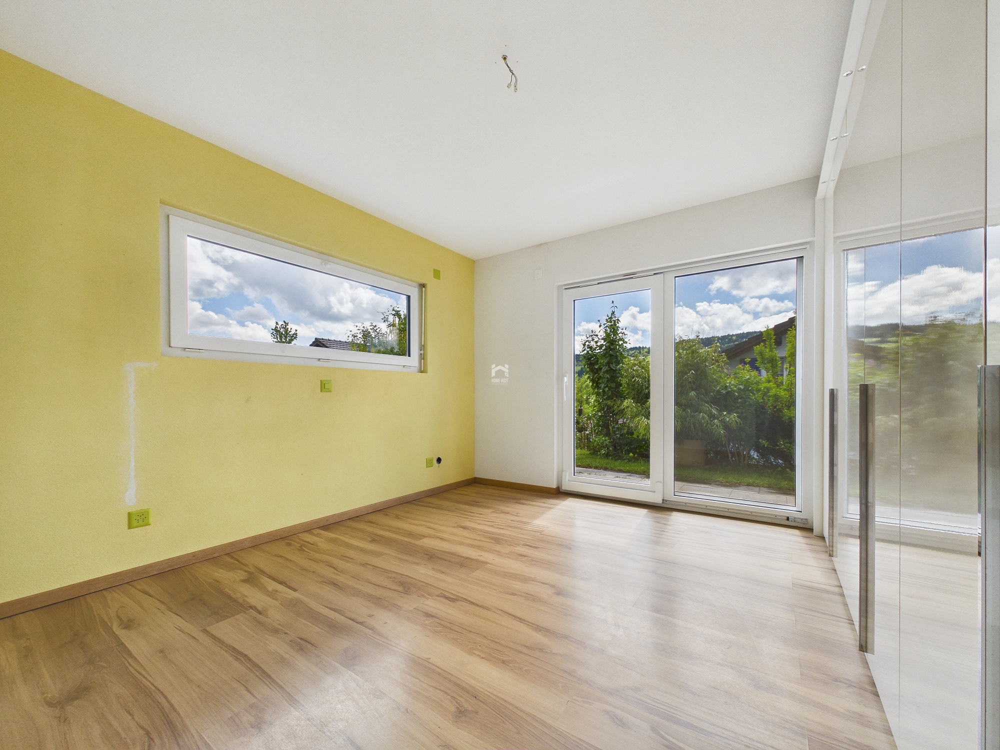 Heller leerer Raum mit Fenstern und Holzoptik-Boden