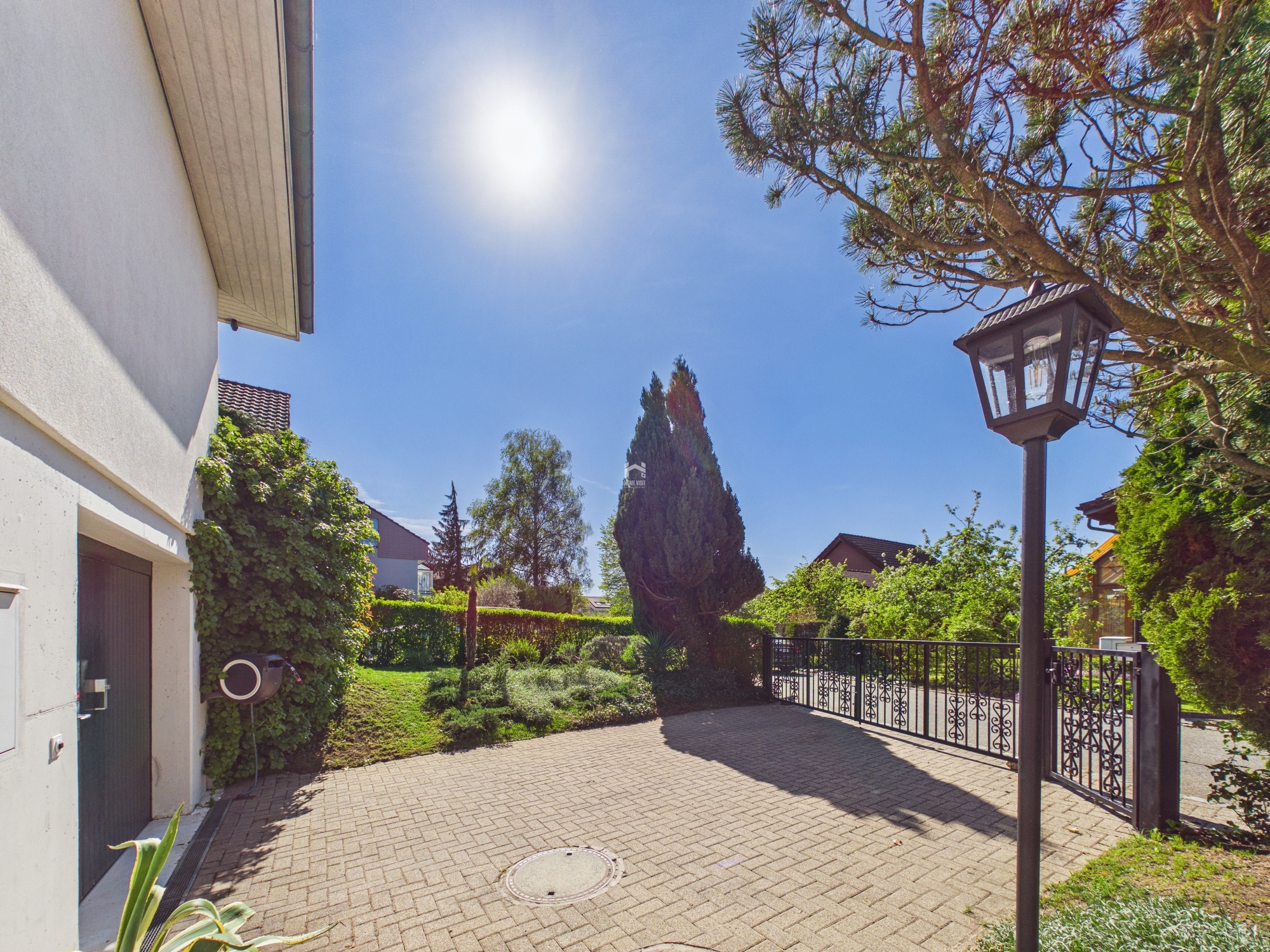Sonnige Außenansicht mit gepflasterter Hofeinfahrt und Garten