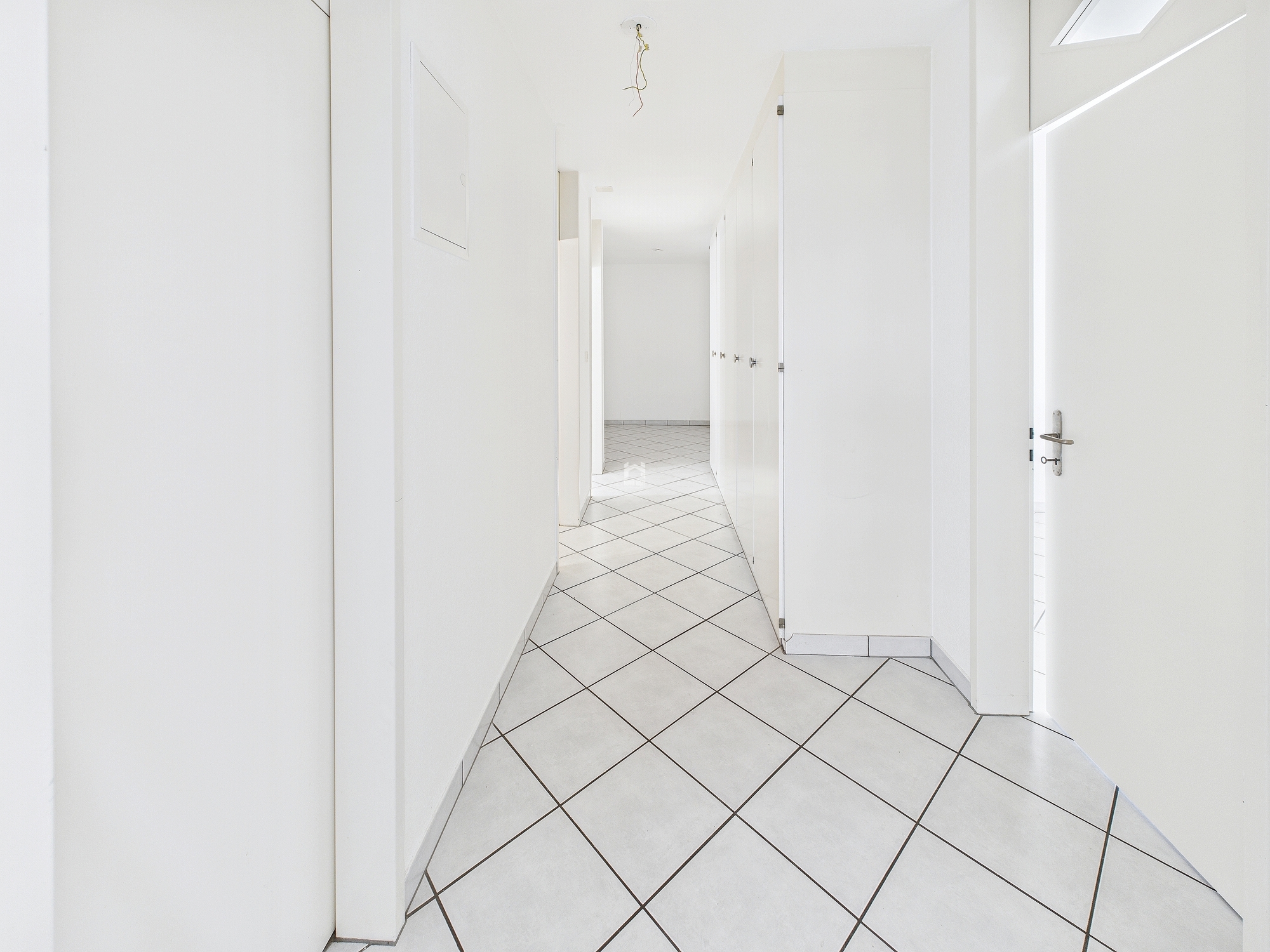 Heller Flur mit weißen Türen und diagonalen Bodenfliesen