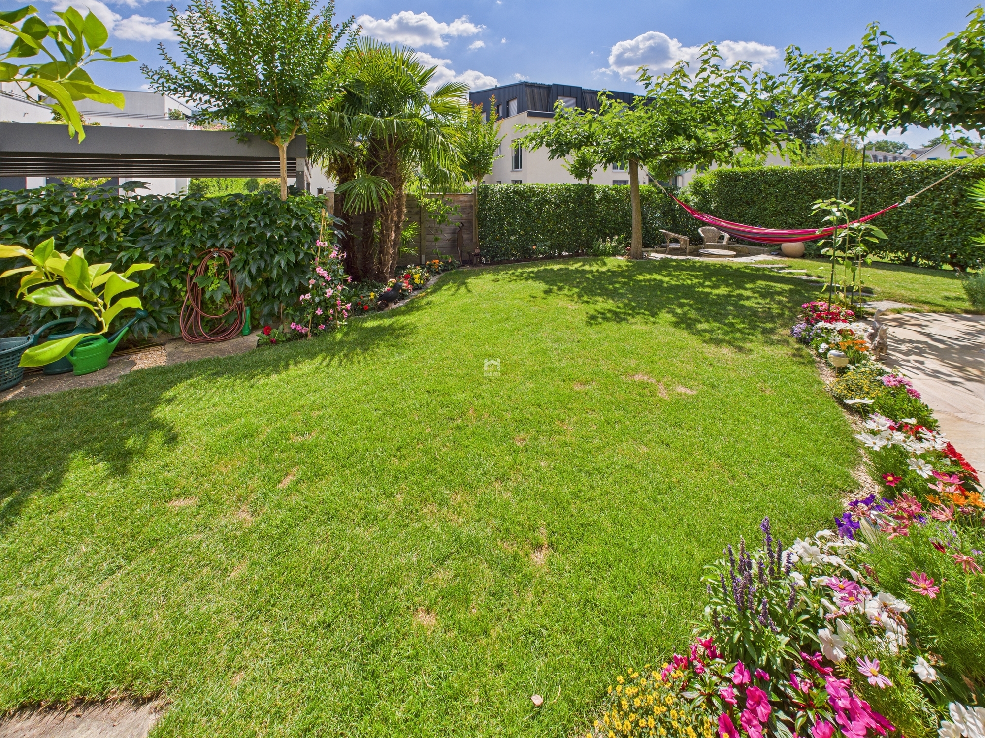 Großer, gepflegter Garten mit Rasen, Blumenbeeten und Hängematte