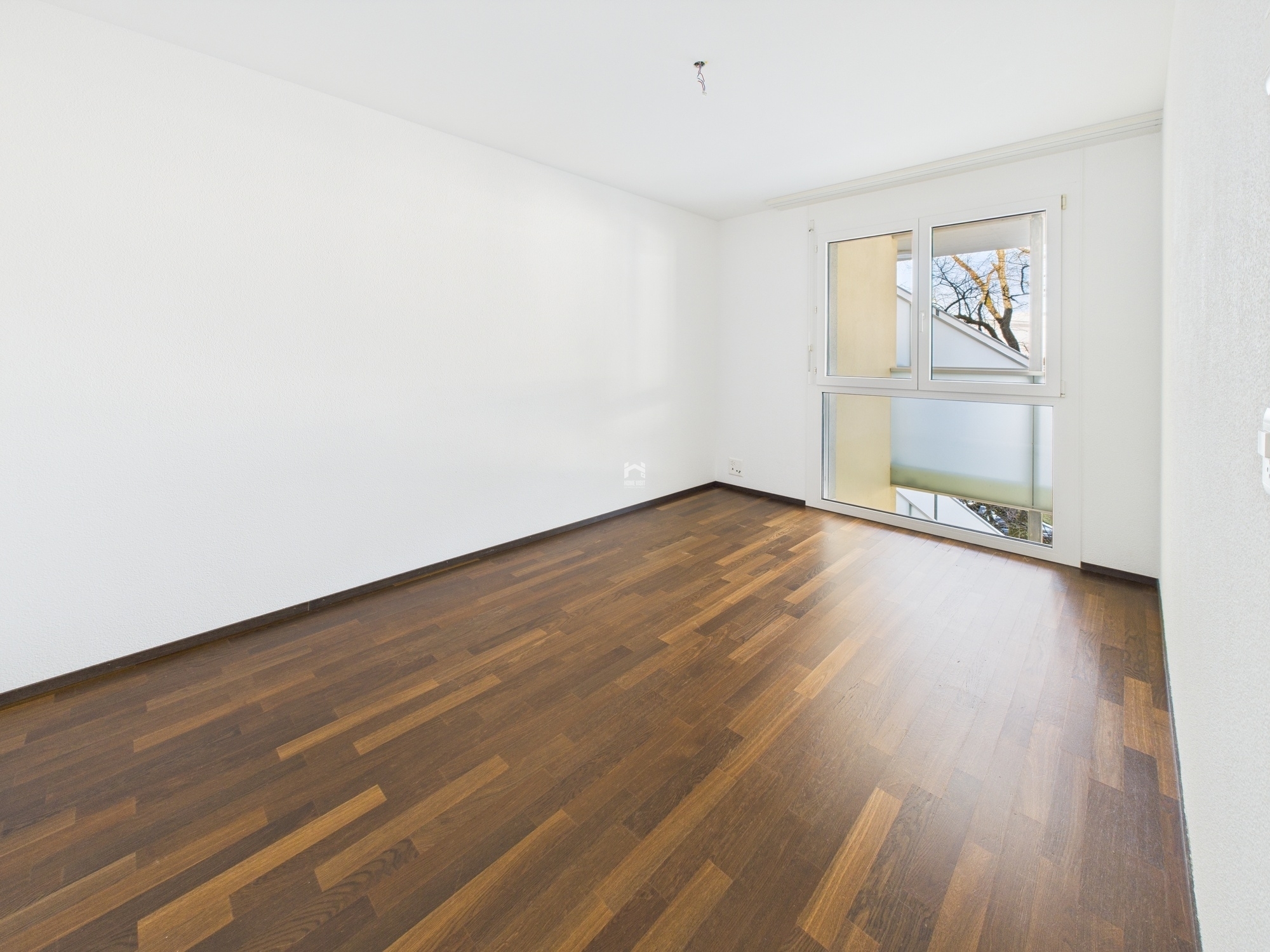 Heller leerer Raum mit Holzboden und großem Fenster