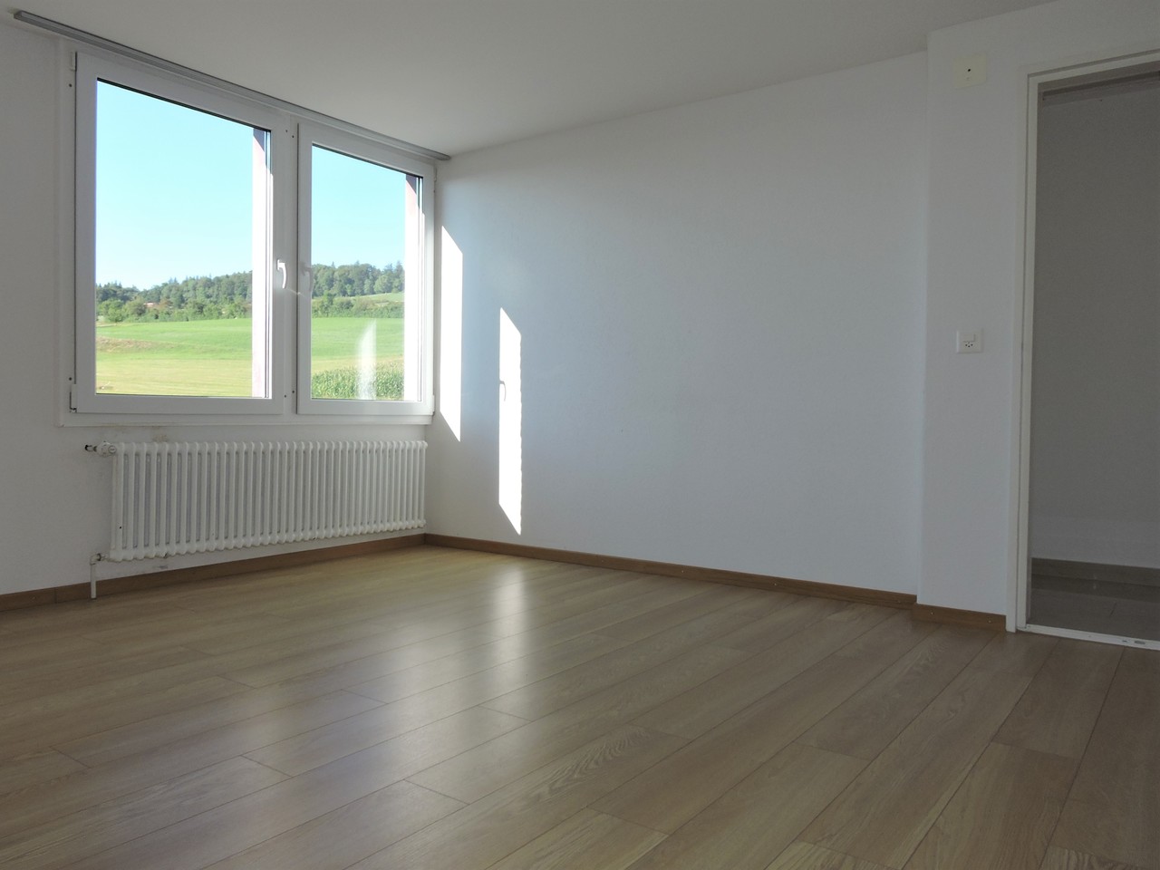 Leeres, helles Zimmer mit Fensterblick ins Grüne