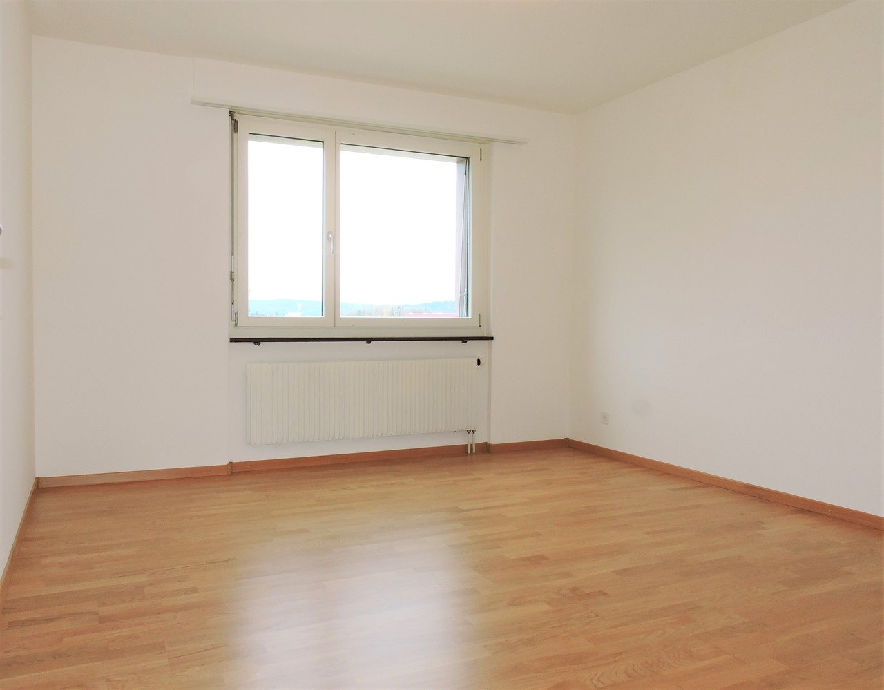 Leerer, heller Raum mit Holzoptik-Boden und Fenster