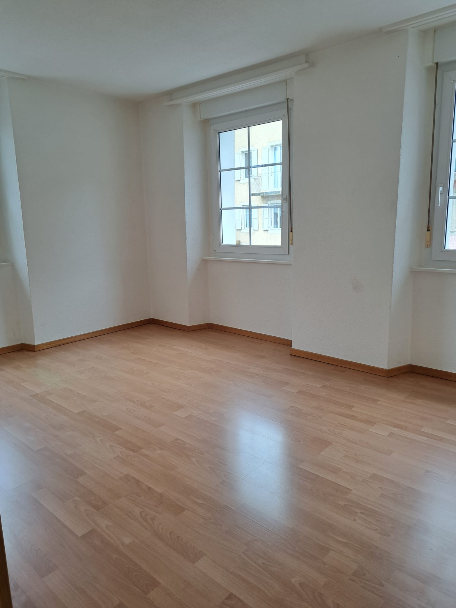 Heller leerer Wohnraum mit Laminatboden und Fenstern