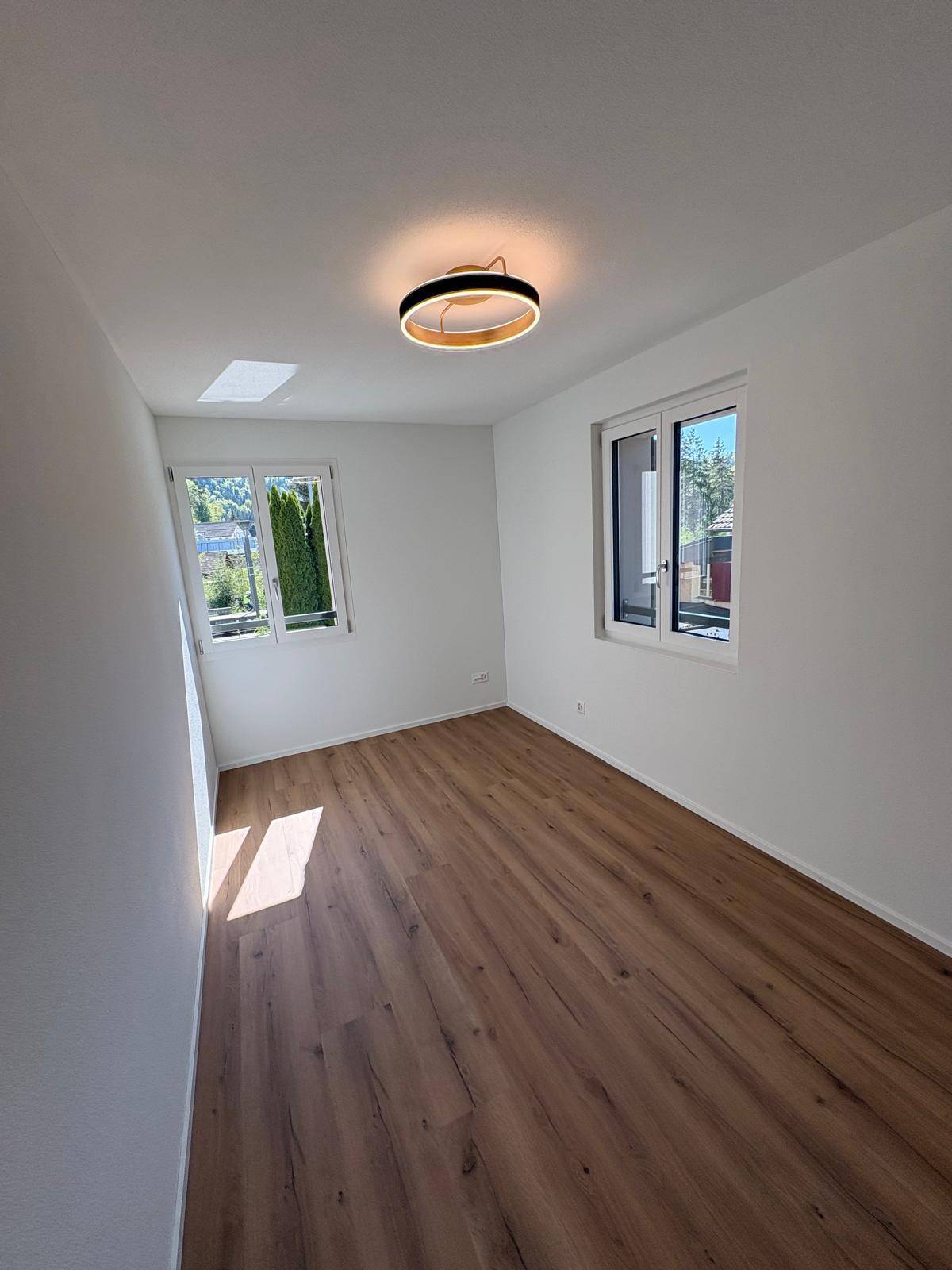 Heller leerer Raum mit Holzoptik-Boden und zwei Fenstern