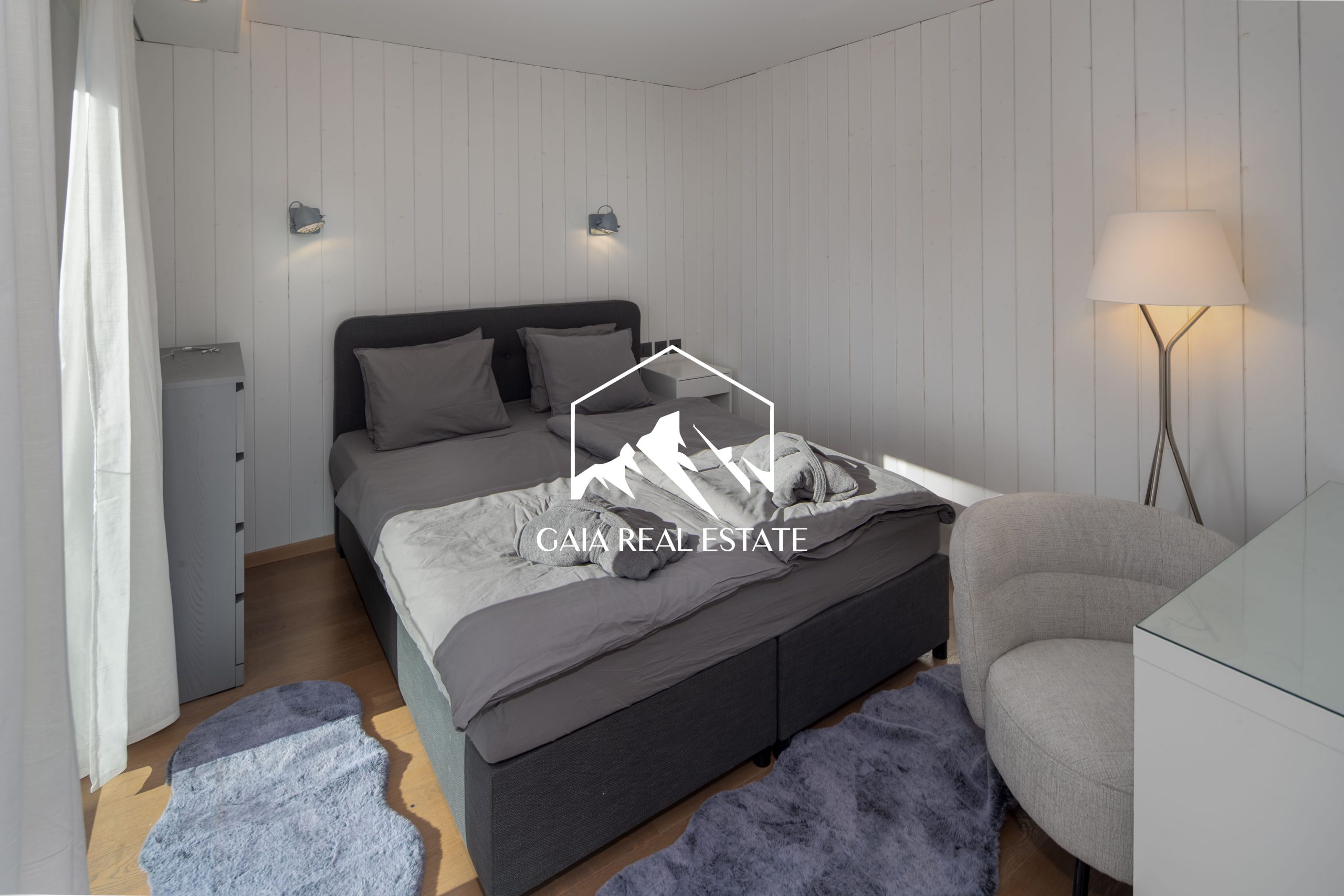 Helles Schlafzimmer mit grauem Bett und heller Holzvertäfelung