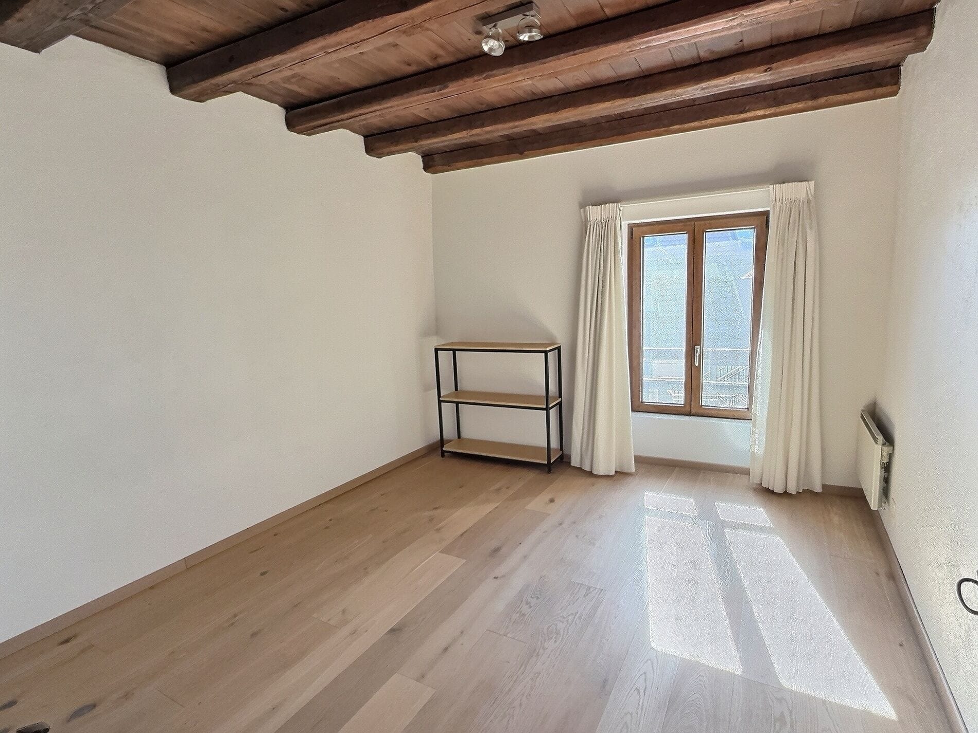 Helles, leer geräumtes Zimmer mit Holzbalkendecke
