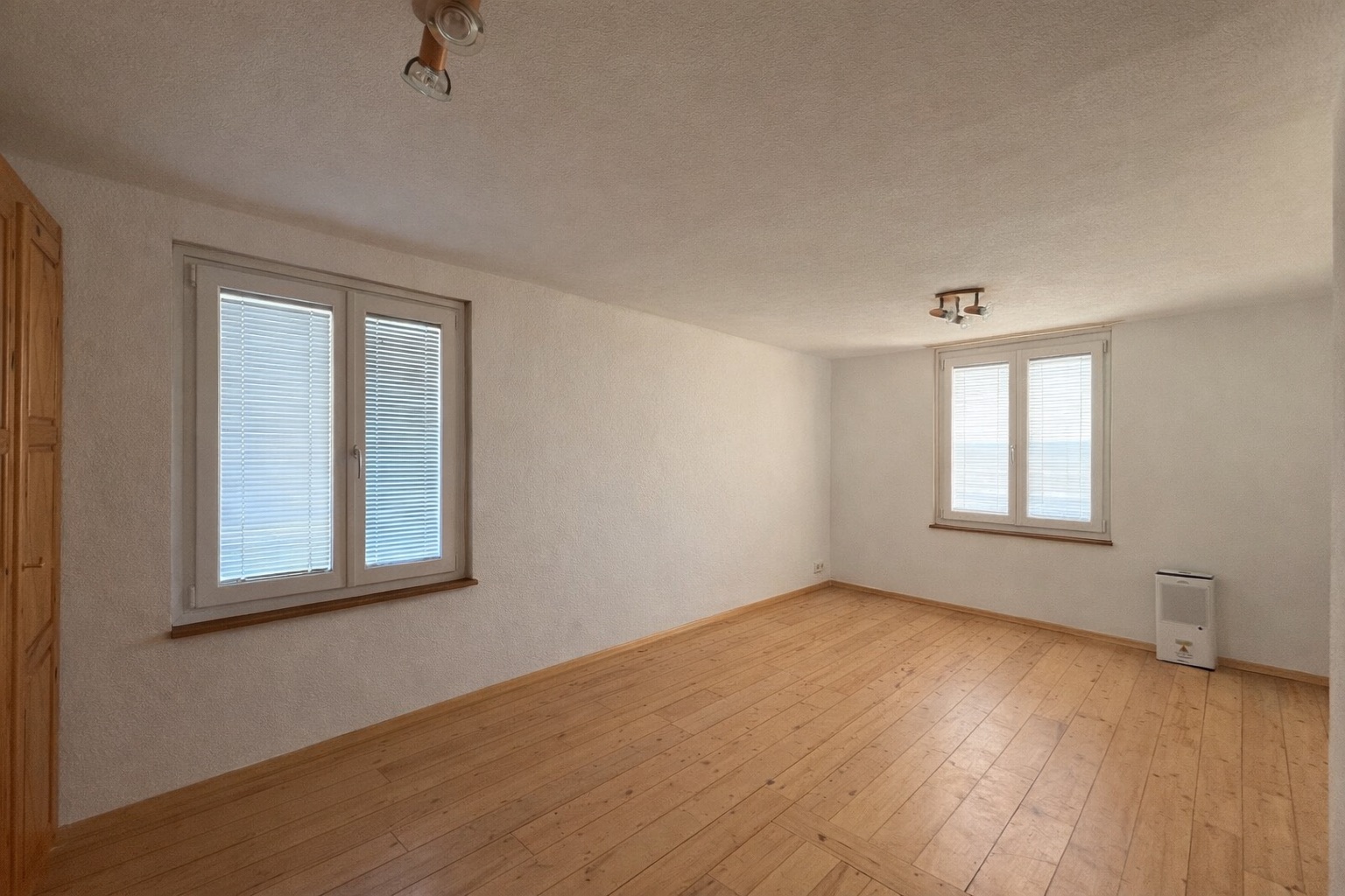 Leerer Wohnraum mit Holzboden und zwei Fenstern