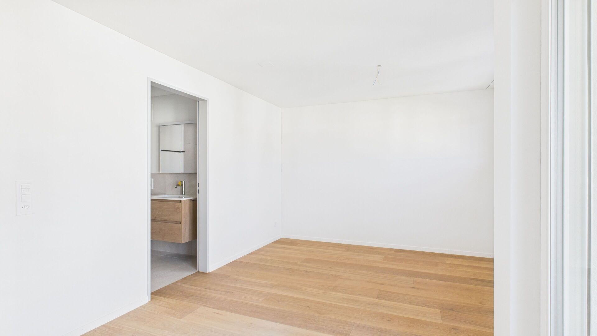 Helles, leeres Zimmer mit Blick in einen angrenzenden Sanitärbereich