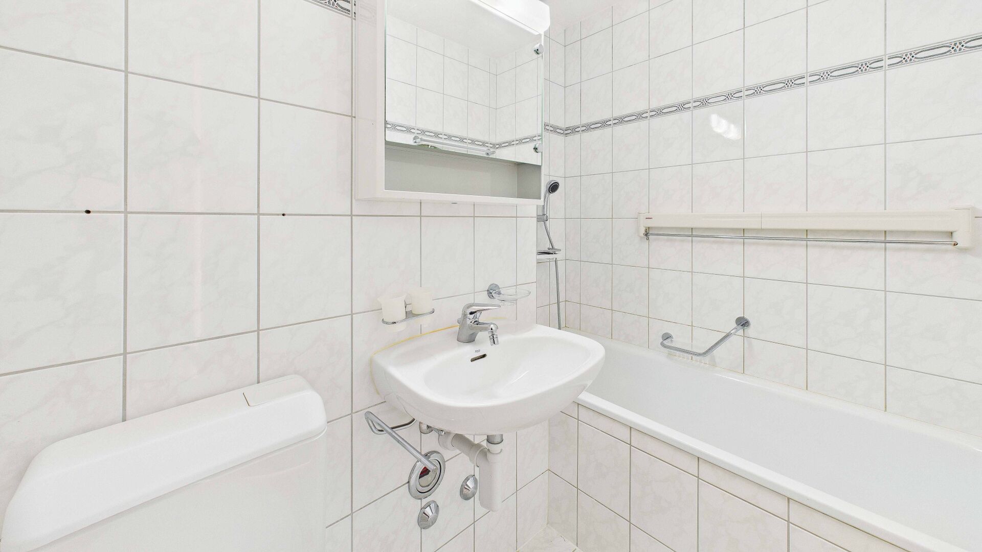Kleines weiß gefliestes Badezimmer mit Badewanne und Waschbecken