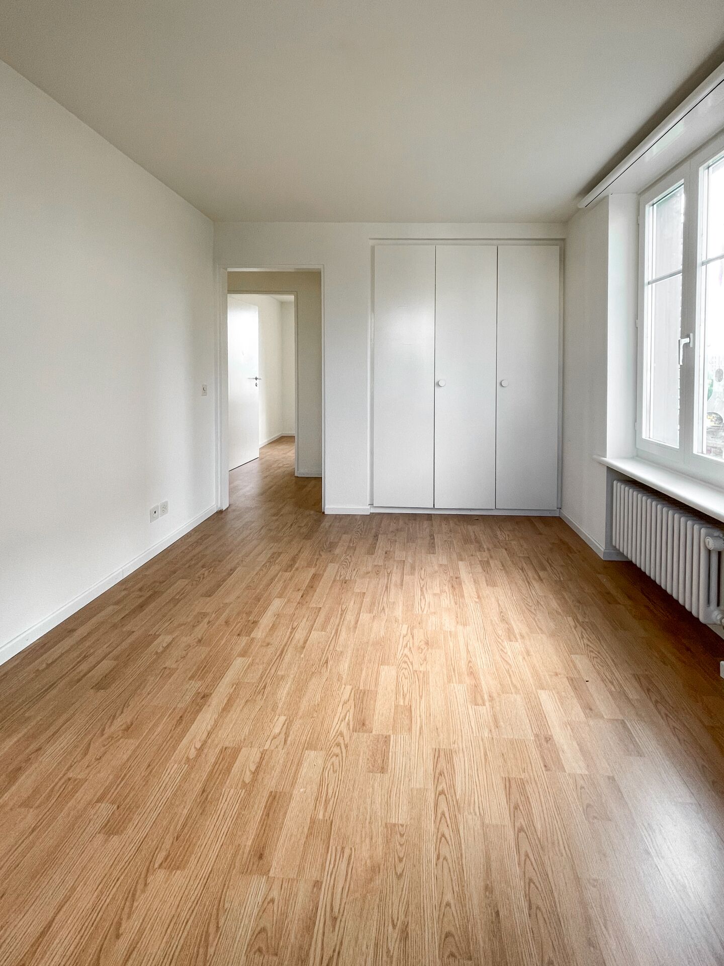 Helles, leeres Zimmer mit Parkettboden und Einbauschrank