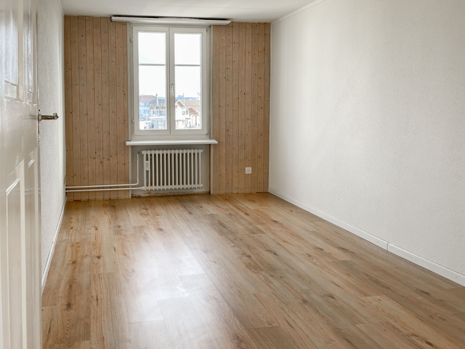 Heller leerer Raum mit Holzoptik-Boden und Fenster