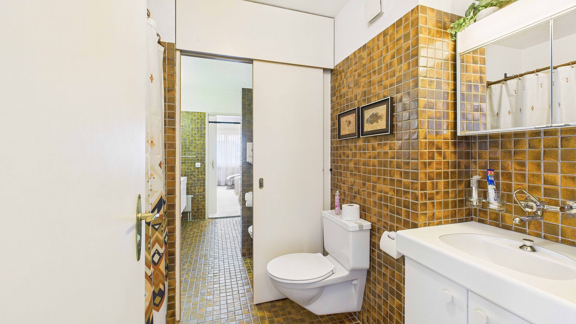 Retro-Bad mit Goldfliesen und wandhängendem WC