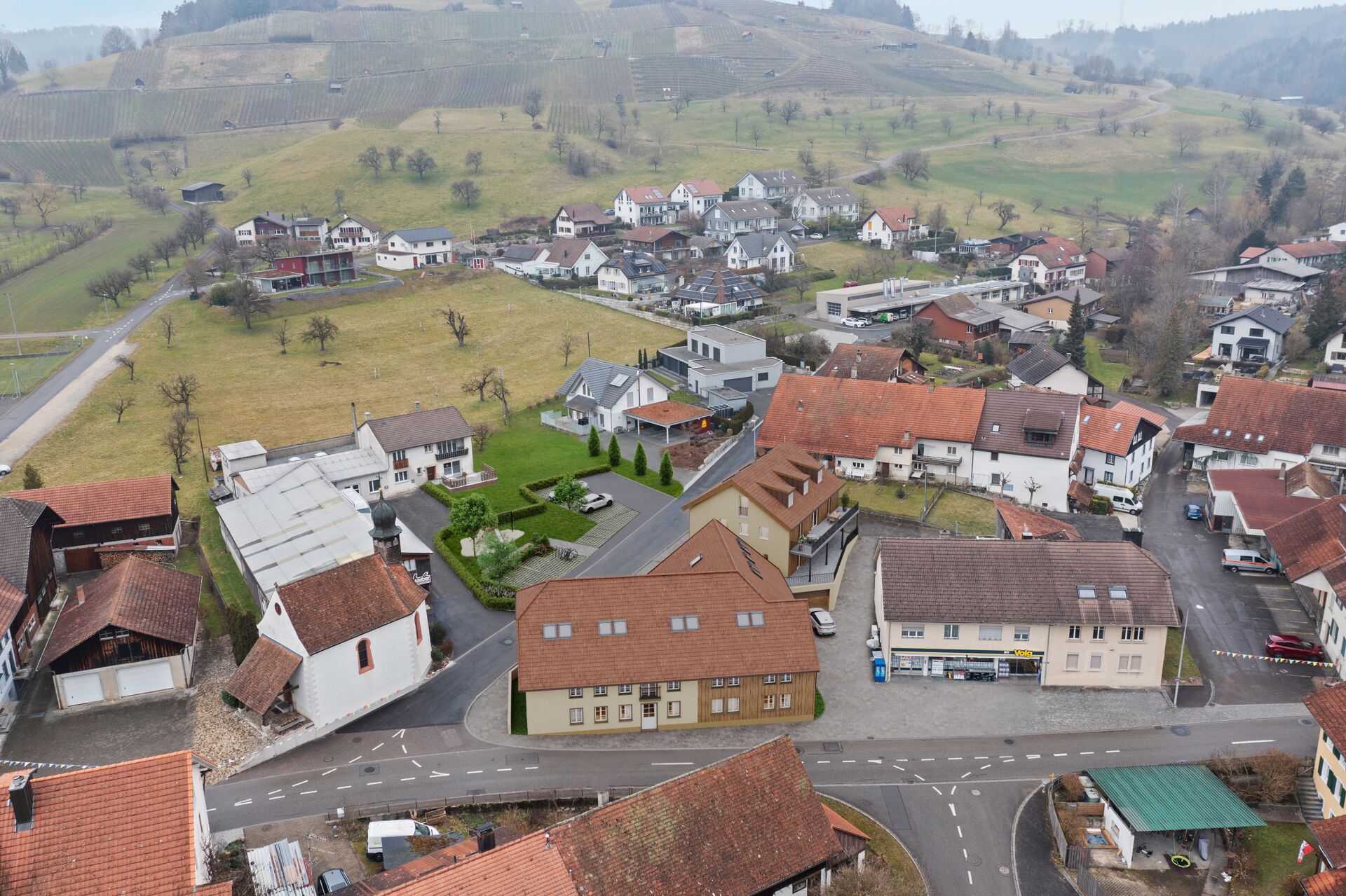 Luftaufnahme eines Dorfkerns in hügeliger Landschaft