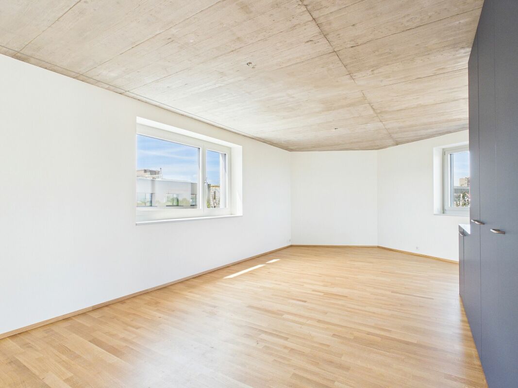 Helles, leeres Wohn- oder Schlafzimmer mit Holzparkett und Sichtbetondecke