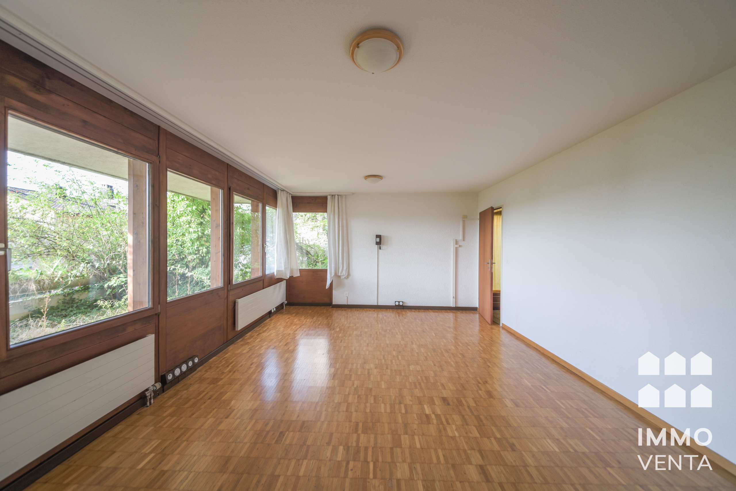 Heller, leerer Wohnraum mit großen Holzfenstern