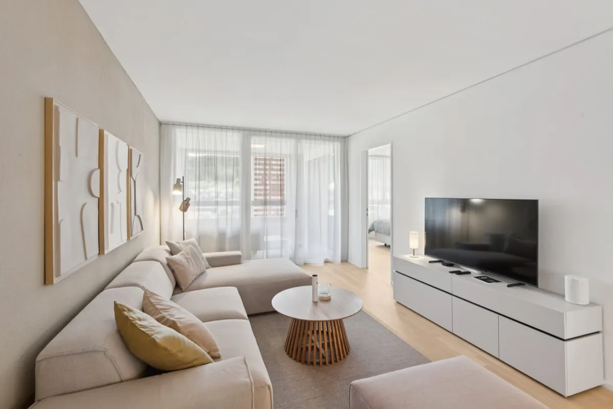 Heller, moderner Wohnraum mit Sofa, TV und Balkonzugang
