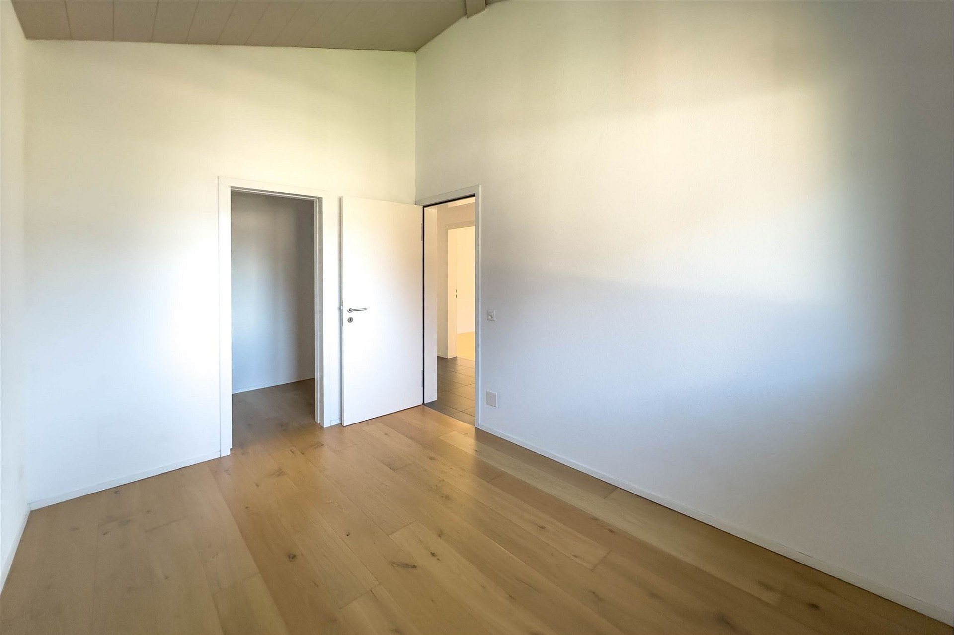 Helles, leeres Zimmer mit Holzboden und zwei Türen