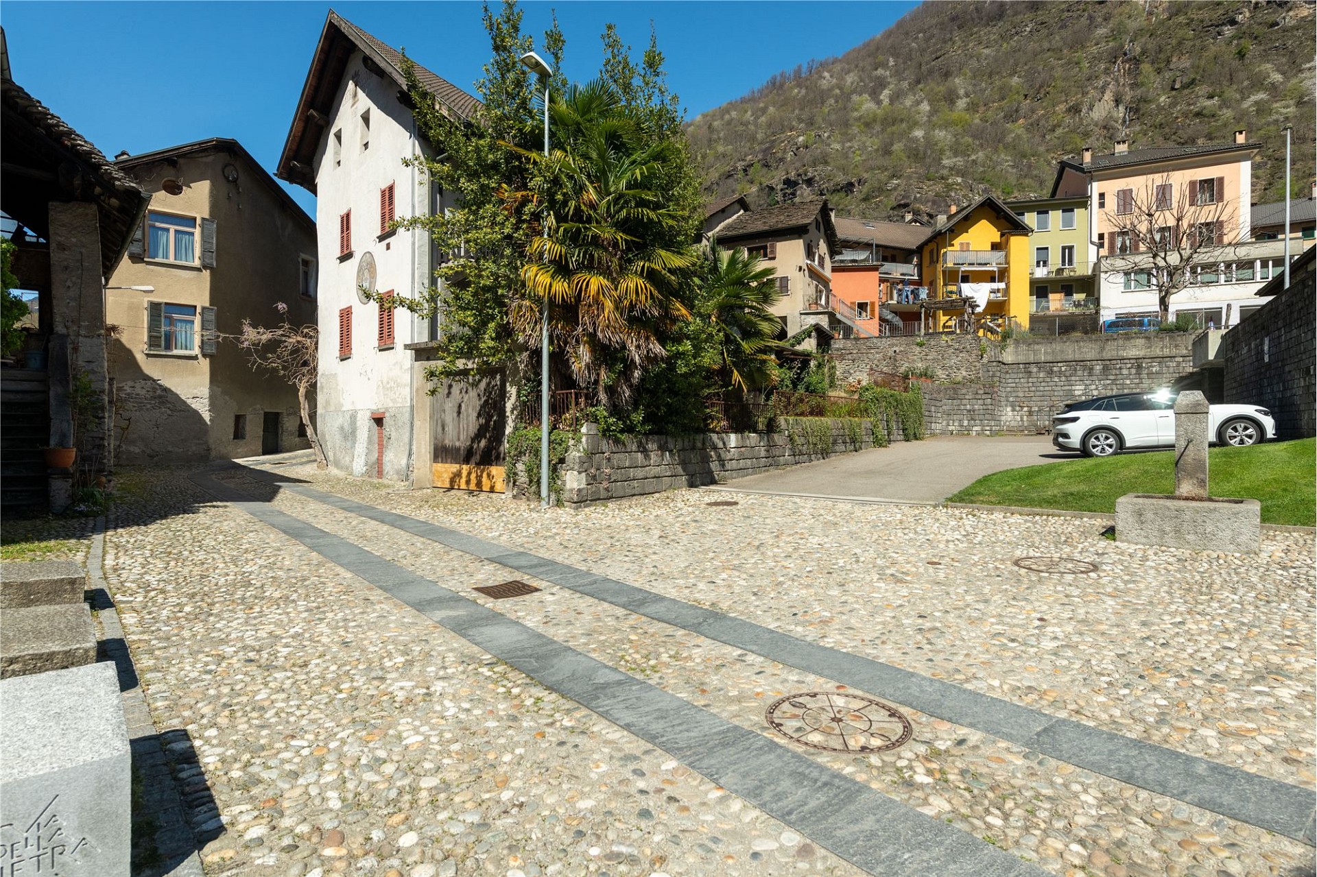 Dorfplatz mit Wohnhäusern und Bergkulisse