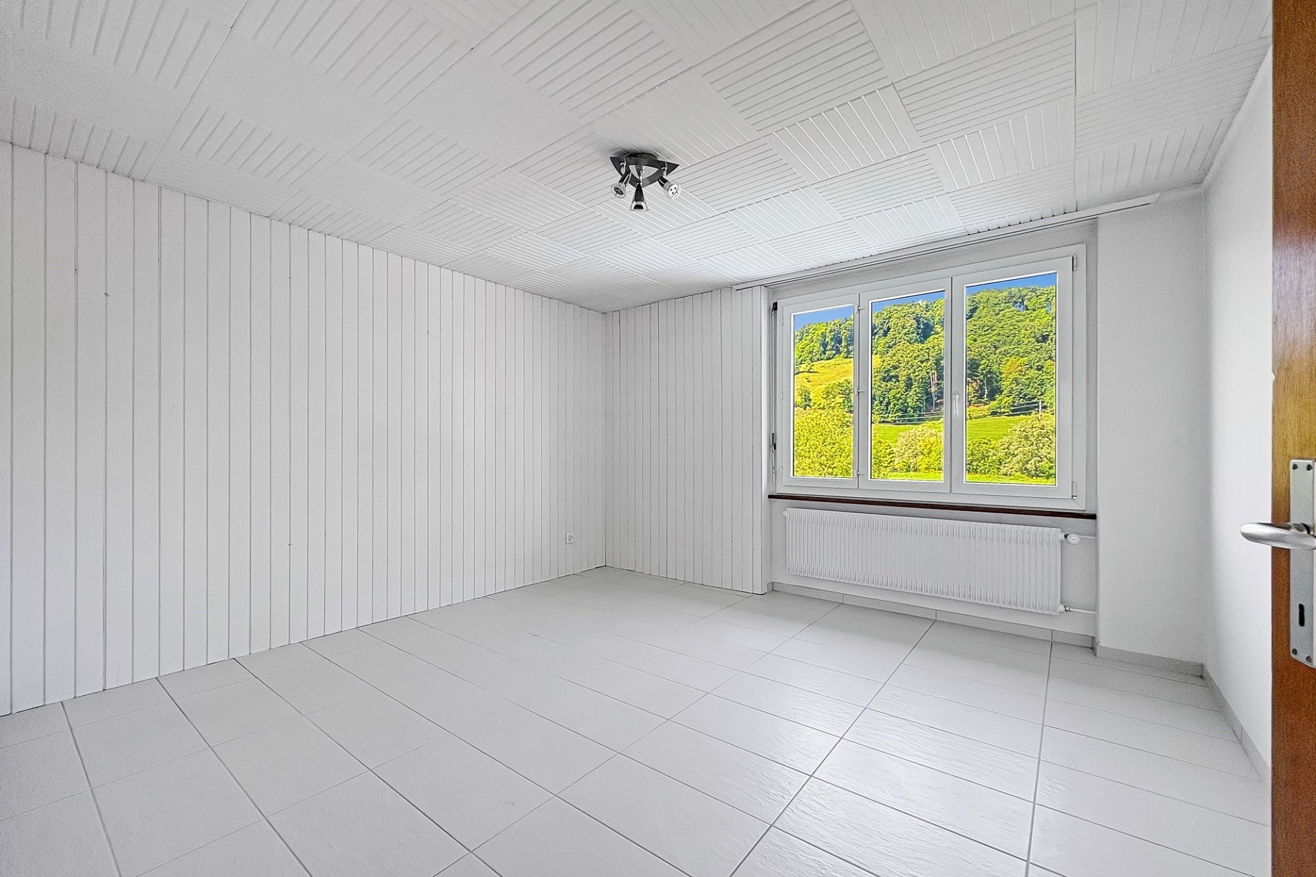 Leerer heller Raum mit Fliesenboden und Fensterblick ins Grüne