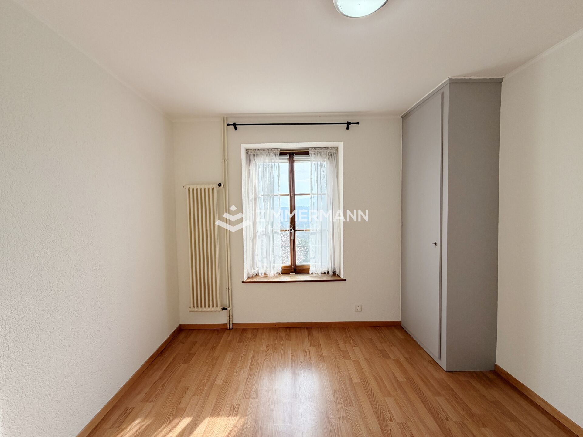 Helles, schlichtes Zimmer mit Fenster und Heizkörper