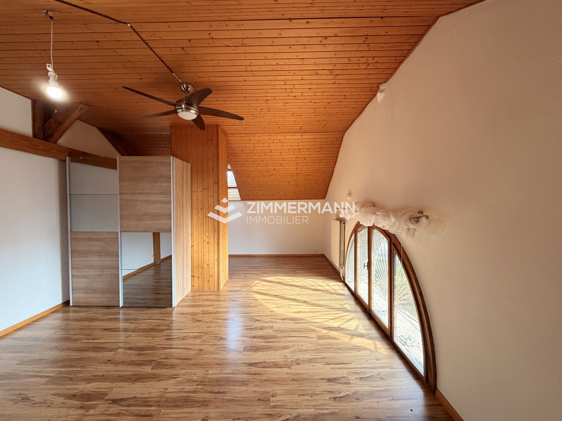 Dachgeschossraum mit Holzdecke und großem Bogenfenster