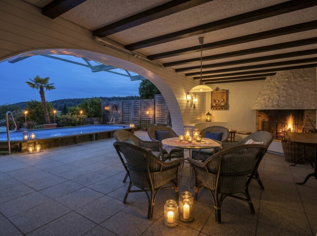 Überdachte Terrasse mit Pool und Kamin bei Dämmerung