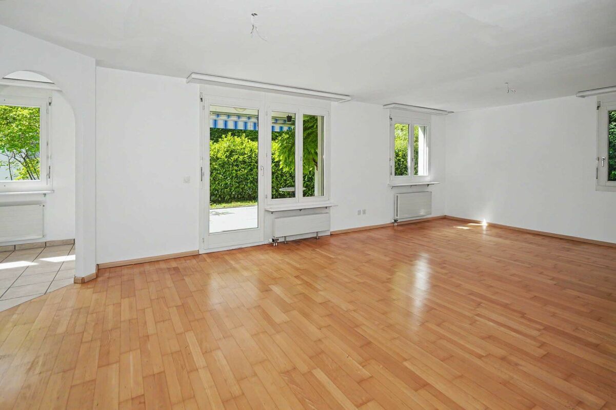 Heller leerer Wohnraum mit Holzboden und mehreren Fenstern