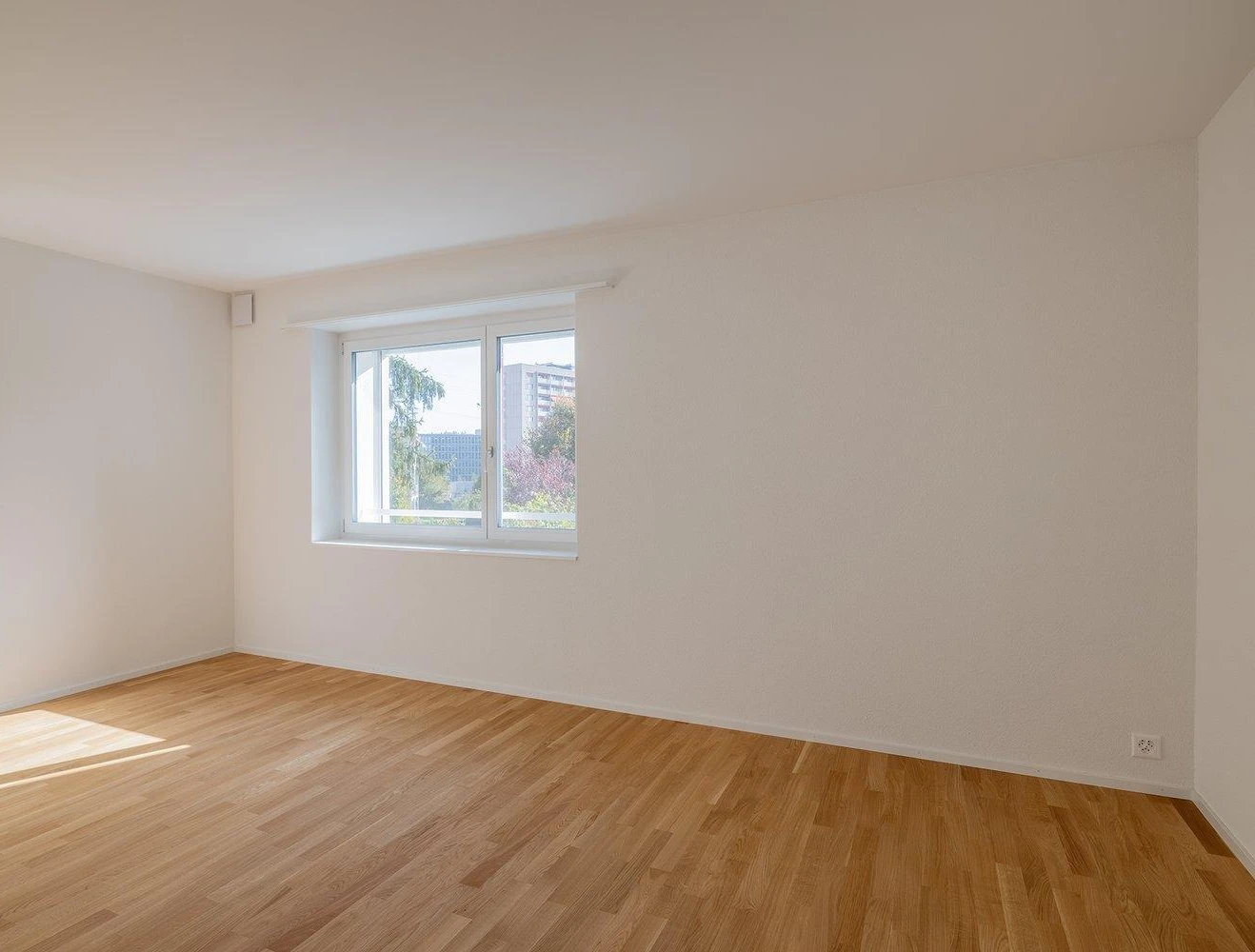 Helles, leeres Zimmer mit Holzfußboden und Fenster