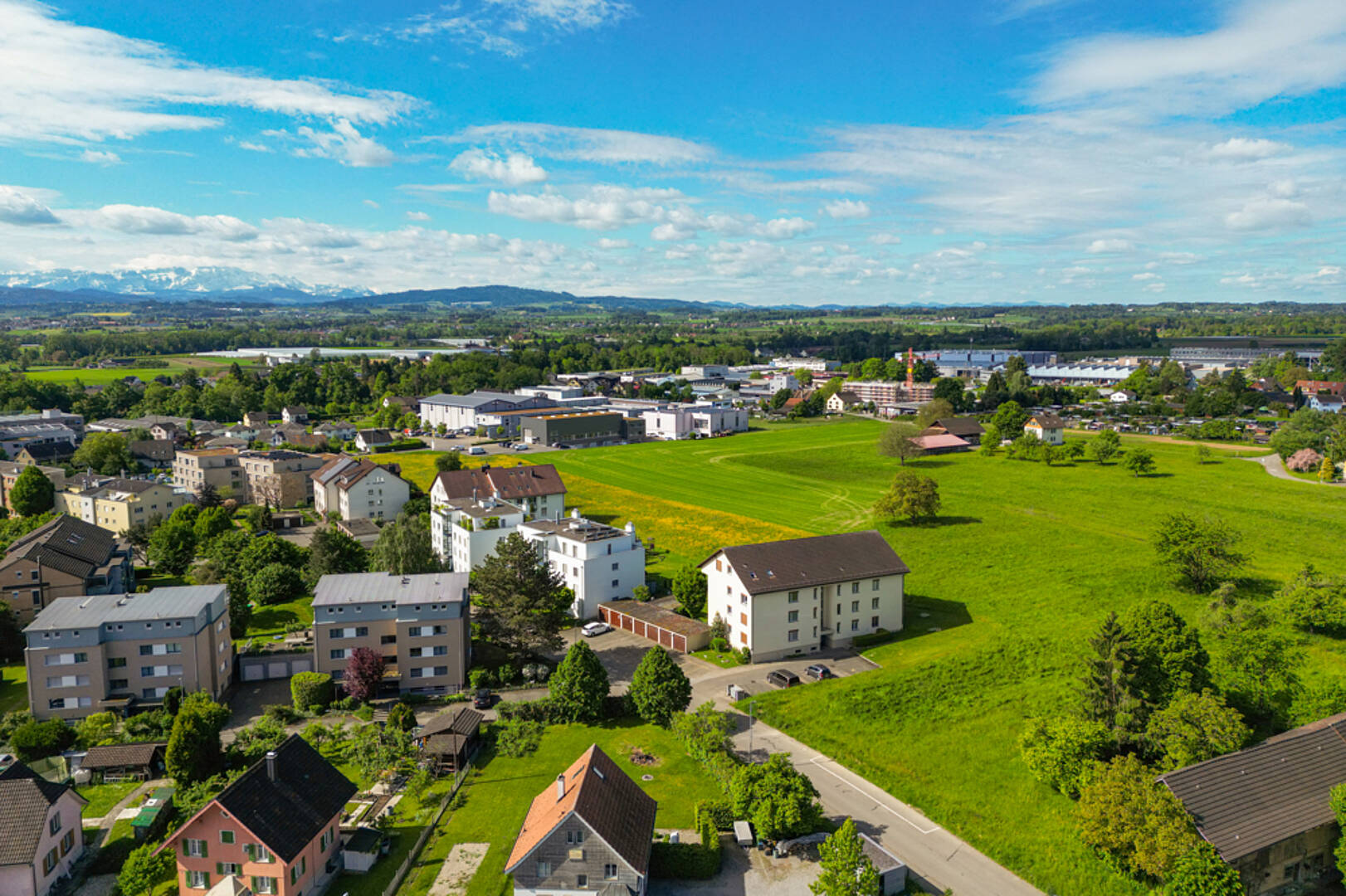 Luftaufnahme einer Wohnsiedlung mit Grünflächen und Bergblick