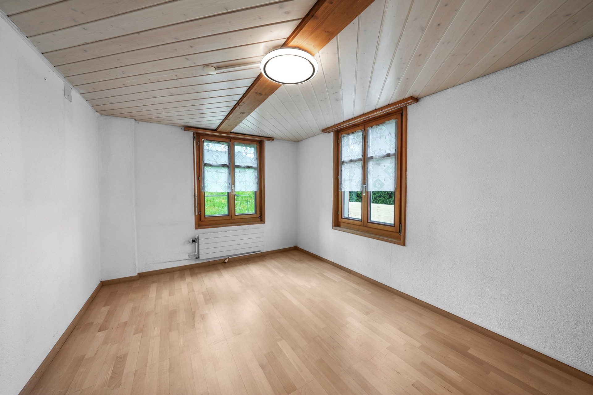 Leerer Raum mit Holzdecke und zwei Fenstern