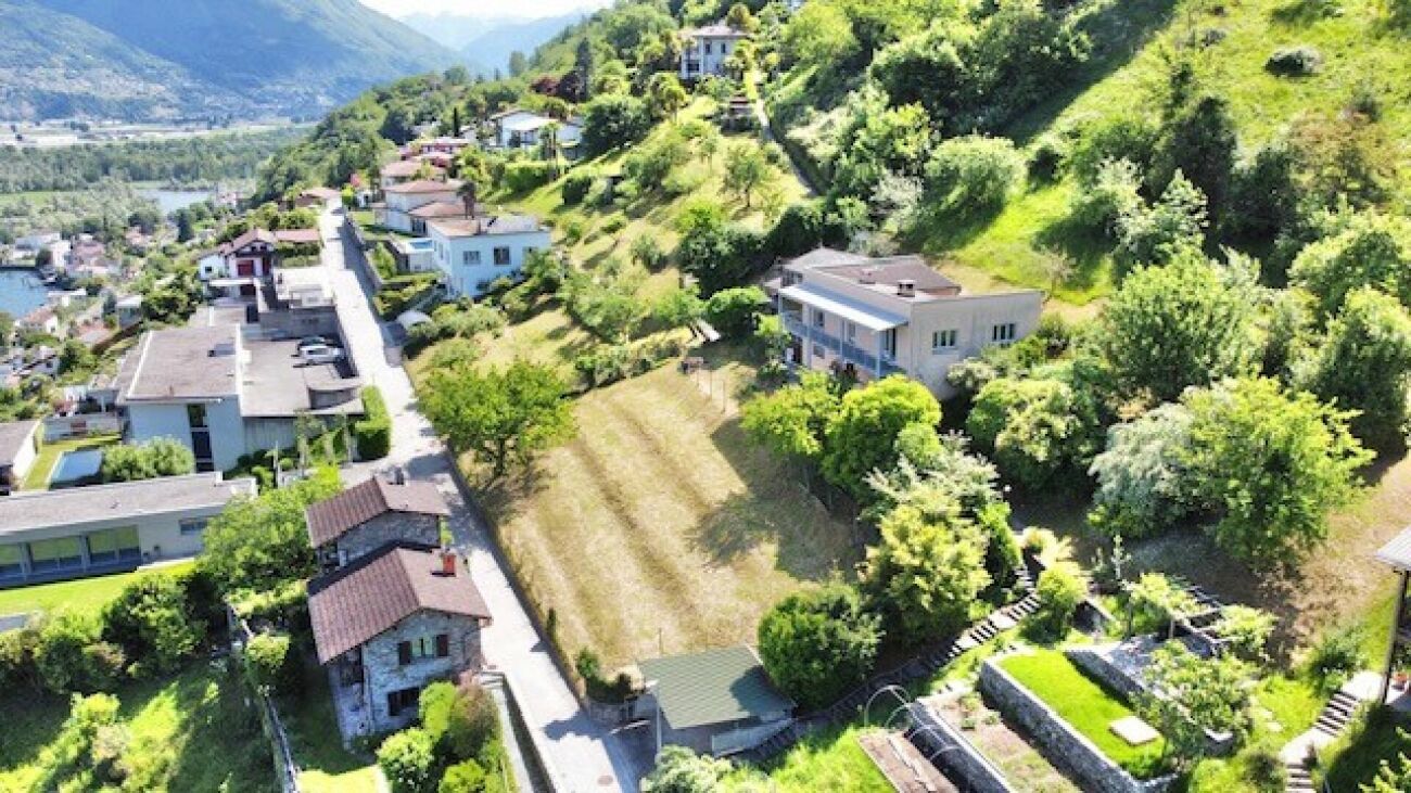 Luftaufnahme eines grünen Hanggrundstücks mit Wohnhäusern und Talblick