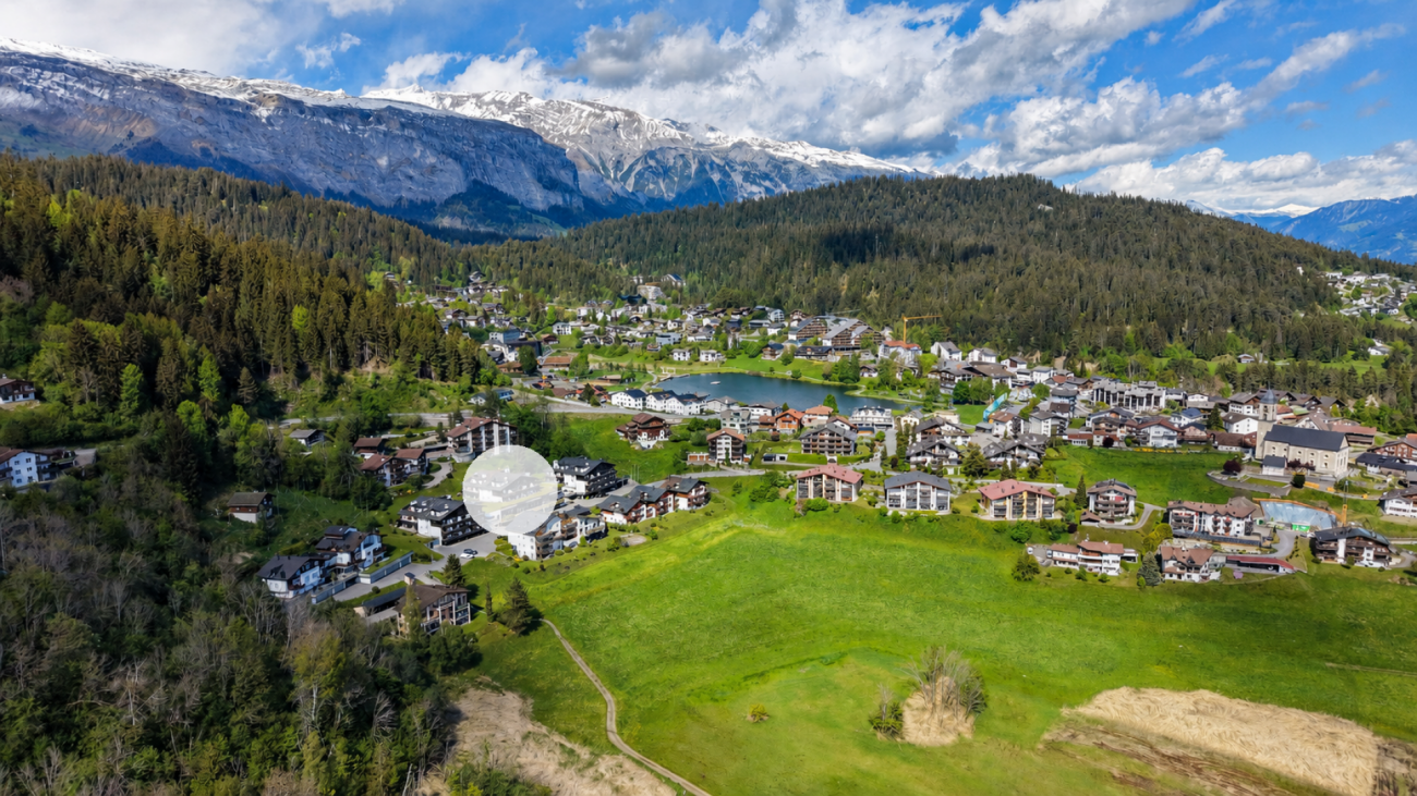 Luftaufnahme eines Bergortes mit See und Alpenpanorama