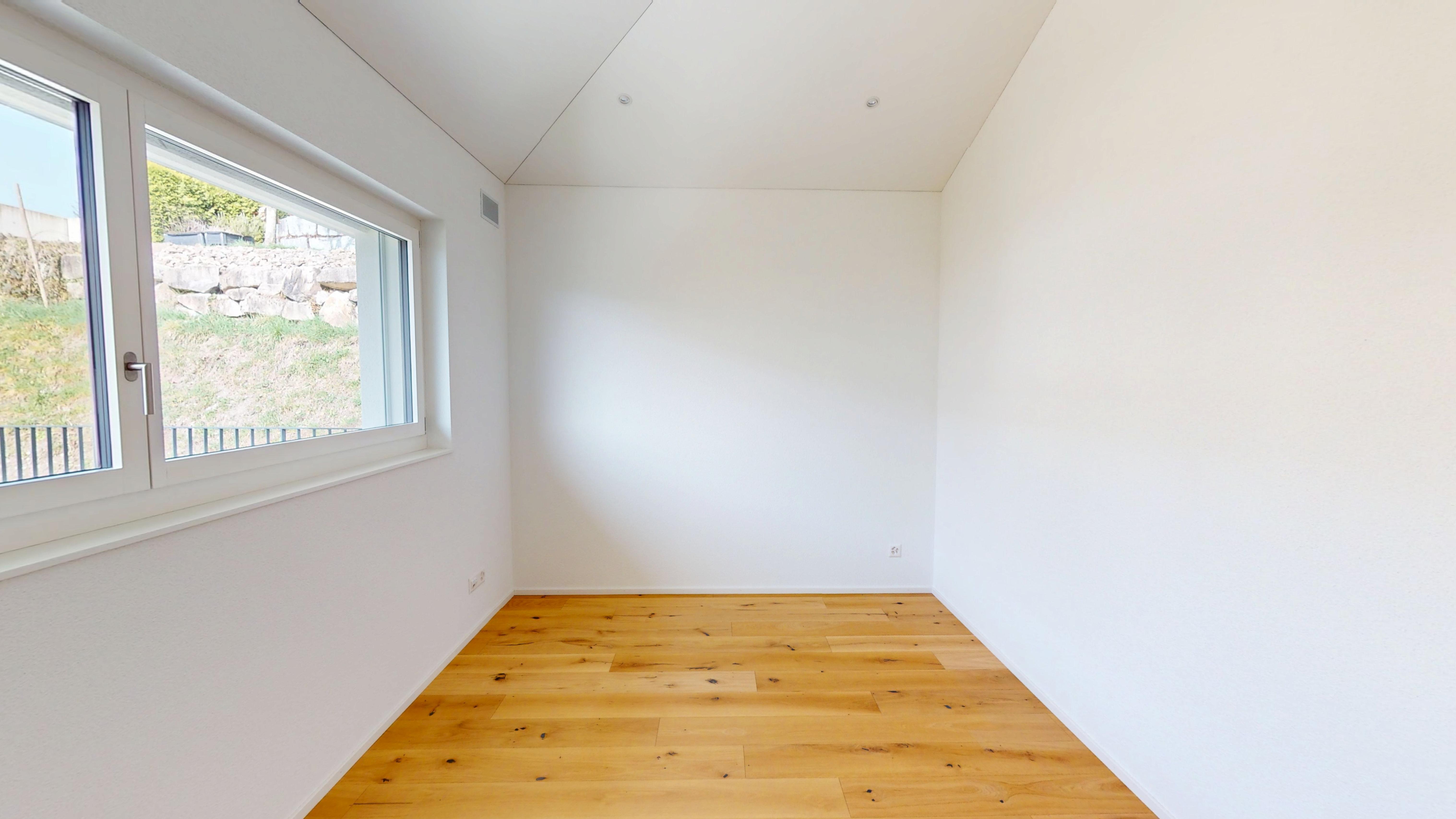 Helles, leeres Zimmer mit Holzboden und Fensterblick ins Grüne