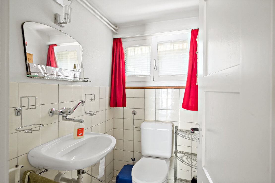 Kleines WC mit Fenster und roten Vorhängen