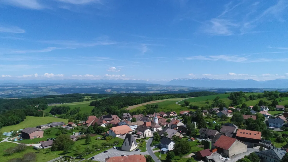 Luftaufnahme einer ländlichen Siedlung mit Alpenpanorama