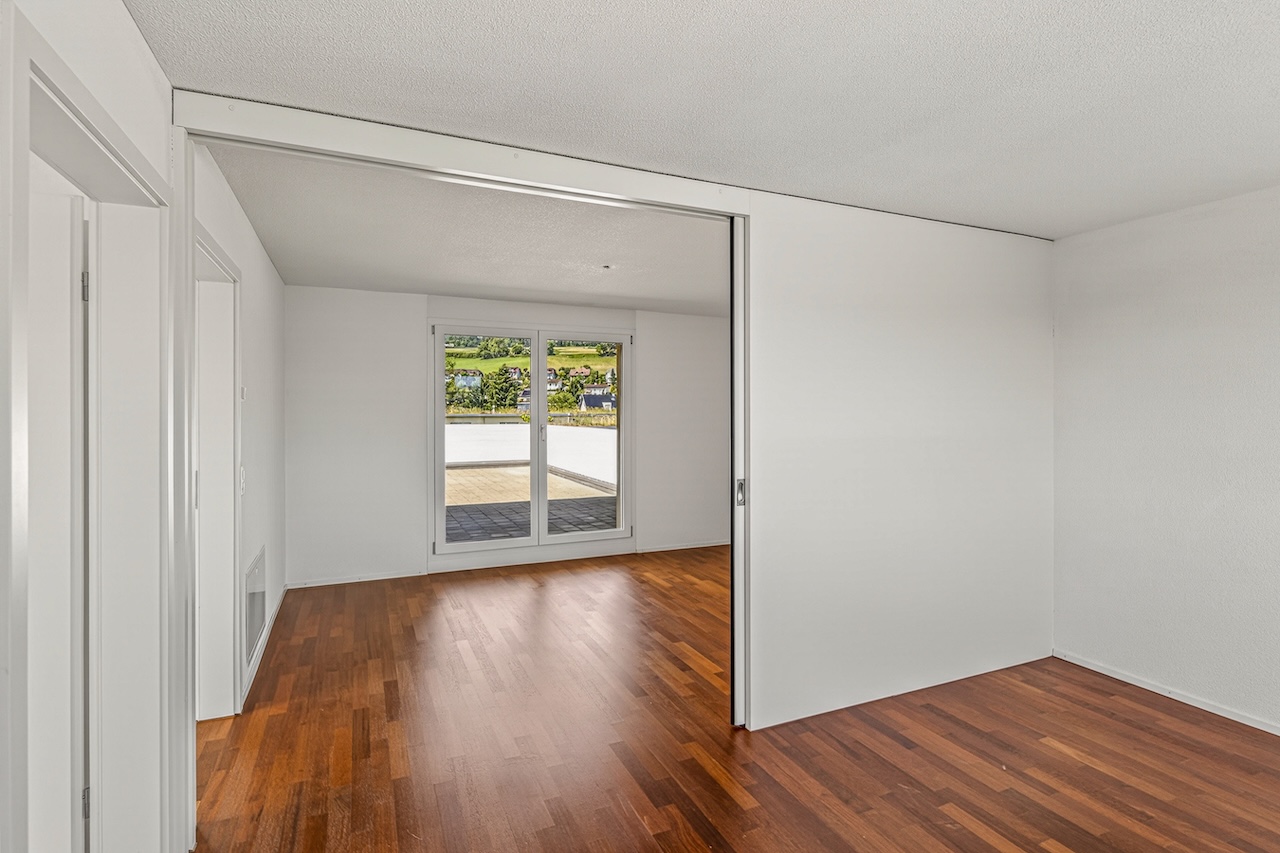 Heller leerer Wohnraum mit Parkett und Schiebetür zum Balkon